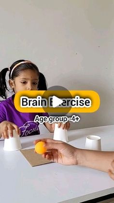 two children are sitting at a table and one is playing with an orange in front of the other