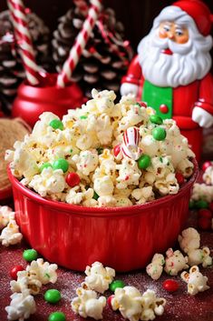 a red bowl filled with christmas popcorn next to candy canes and peppermints