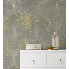 a white dresser sitting next to a wall with gold stars on it and a vase