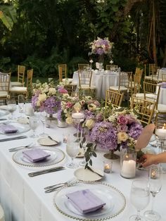 a long table is set with purple and white floral centerpieces, silverware, and candles