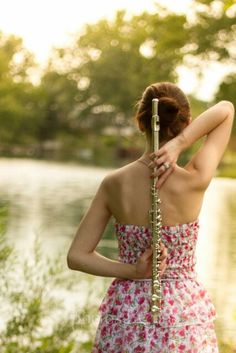 a woman in a floral dress holding a flute by the water's edge with her hands behind her head