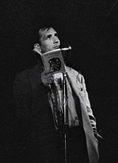 a man standing in front of a microphone holding a book