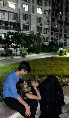 two young people sitting on the steps in front of a building at night, one is looking at his cell phone