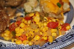 a blue and white plate topped with meat, vegetables and corn on the cob