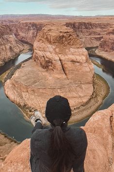 a person standing on top of a cliff overlooking a river and canyon area with mountains in the background