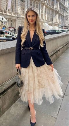 a woman is standing on the sidewalk wearing a skirt and jacket