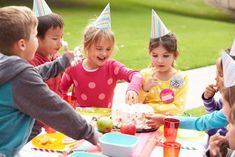 a group of children sitting around a table with birthday hats on top of their heads