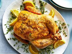 a whole chicken on a plate with lemons and herbs