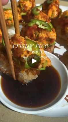 a person is holding chopsticks over some food on a white plate with brown sauce