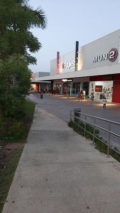 an empty sidewalk in front of a store with people walking on the side walk near it