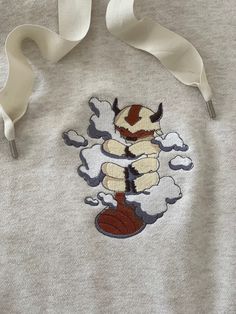 A cream colored sweatshirt with a machine embroidered sky bison named appa. from avatars the last Airbender he is hugging clouds. Avatar The Last Airbender Hoodie, Avatar The Last Airbender Sweatshirt, Appa Embroidery Pattern, Machine Embroidered Clothes, Embroidery Designs On Hoodies, Avatar The Last Airbender Embroidery, Embroidery Avatar, Appa Hoodie