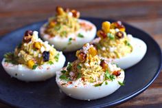 four deviled eggs with various toppings on a black plate