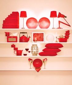 a room with white shelves filled with red items and lamps on the wall above them