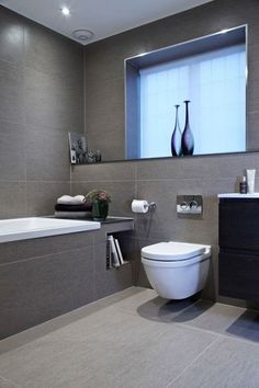 a white toilet sitting next to a bath tub in a bathroom under a large window