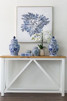 blue and white vases are sitting on a table in front of a framed art piece