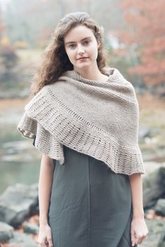 a woman wearing a knitted shawl standing in front of some rocks and trees