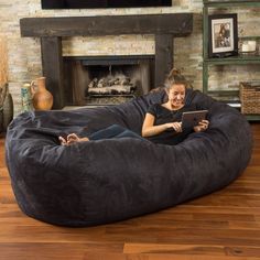 a woman sitting on a large bean bag chair in front of a fireplace with a tablet