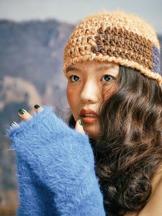 a woman with long brown hair wearing a knitted hat and holding a blue sweater