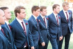 a group of men standing next to each other wearing suits and ties with red flowers on their lapels