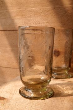 two glasses sitting on top of a wooden table next to each other, one empty