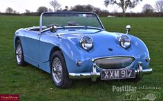 an old blue sports car is parked in the grass