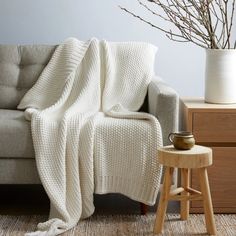 a couch with a blanket on it next to a small table and potted plant