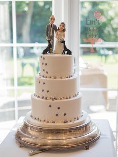 a wedding cake with figurines on top is displayed in front of a window