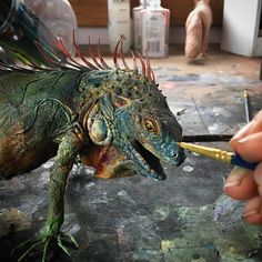 a person is painting an iguana with paintbrushes