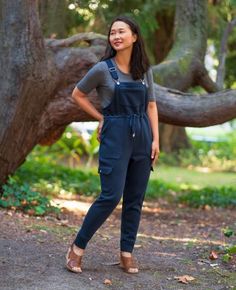 a woman standing in front of a tree with her hands on her hips and smiling