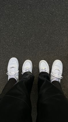 a person wearing white sneakers standing in front of a black floor with his legs crossed