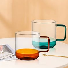 two glass mugs sitting on top of a table next to a magazine and spoon