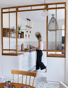 a woman walking through a kitchen next to a table with chairs and shelves on the wall