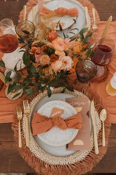 the table is set with an orange and white place setting, gold cutlery, and flowers