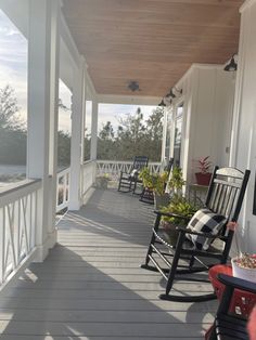 a porch with rocking chairs and potted plants on the front porch, looking out over the water