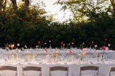 a long table is set with white linens and pink flowers in clear vases