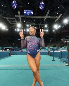 a woman standing on top of a blue floor wearing a leotard and holding her hands up