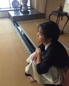 a young woman sitting on the floor in front of a window looking out at something