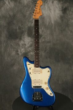 a blue electric guitar sitting on top of a black stand in front of a gray background