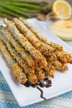 fried asparagus on a white plate with dipping sauce and lemon wedges in the background