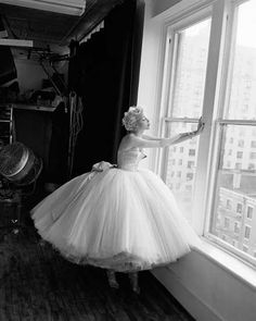 a woman in a white dress standing by a window