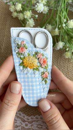 a hand holding a small blue case with flowers on it and two pairs of scissors