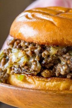 a close up of a hamburger on a wooden plate with text that reads phily cheese steak sloppy joes