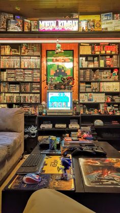 a living room filled with lots of books and video game equipment in front of a tv