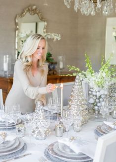 a woman lighting a candle on top of a table with silver christmas tablescapes