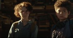 two young boys standing next to each other in front of bookshelves and looking at the camera