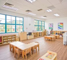 an empty classroom with tables and chairs in front of large windows on the wall, and wooden flooring