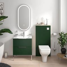 a white toilet sitting next to a green cabinet in a bathroom under a round mirror