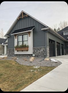 a gray house with two garages and windows on the front side, grass in front of it