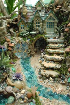 a miniature garden with lots of plants and rocks on the ground in front of a house