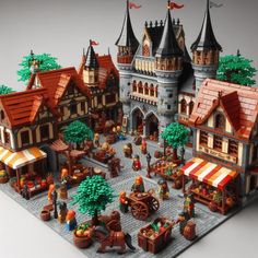 a lego model of a medieval town with lots of buildings and people standing around it